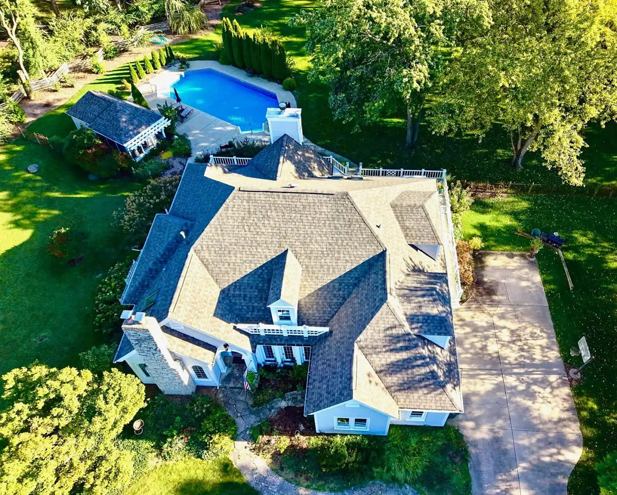 Aerial view of a home with a gray architectural shingle roof, pool and pool house